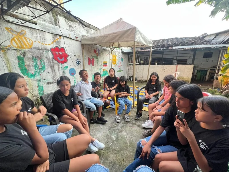 Grupo de niñas y niños sentados en círculo durante un taller al aire libre